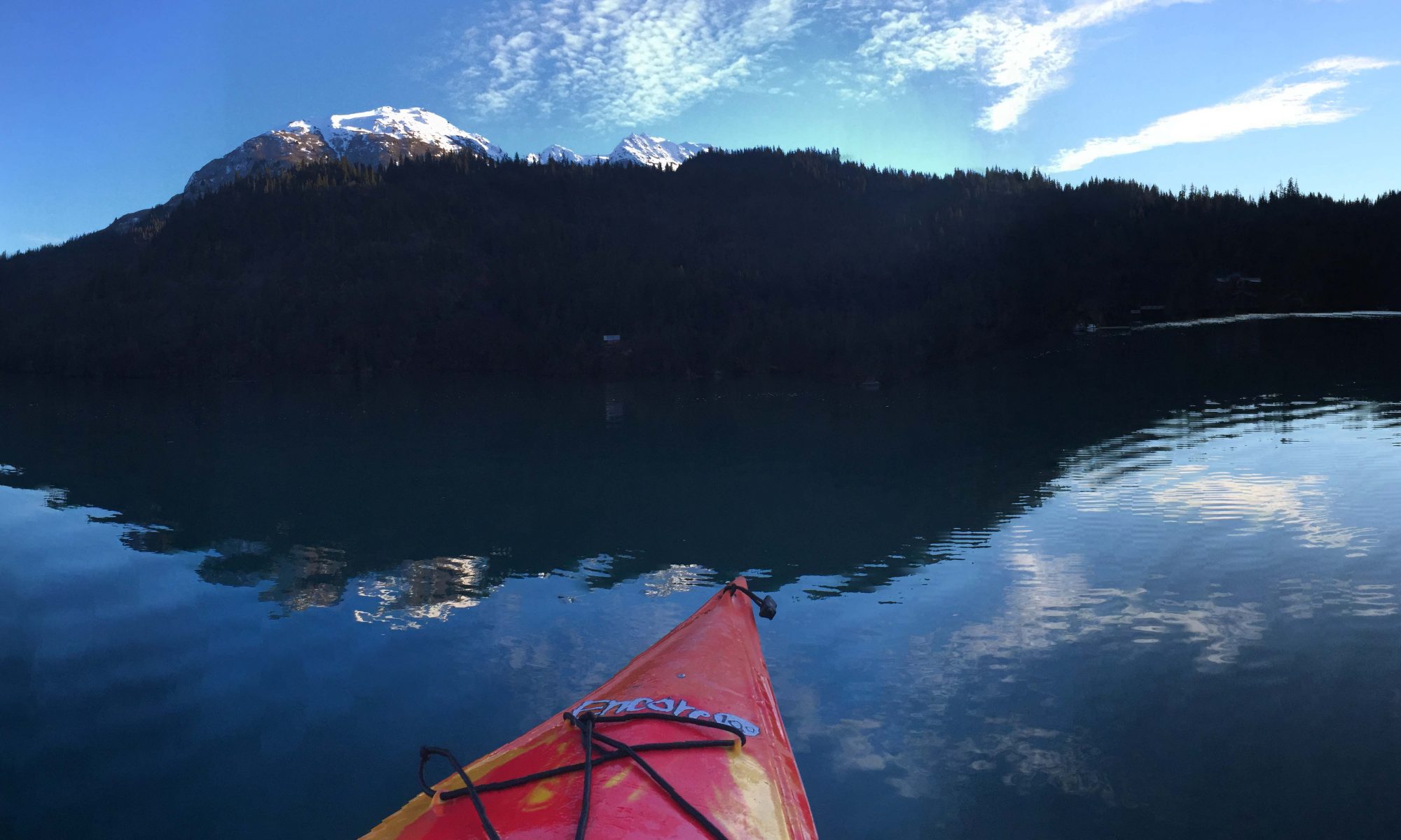 the bow of a kayak against the reflection of mountain on lake